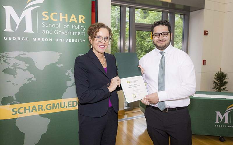 A woman in a dark dress hands a certificate to a man in a white shirt and tie.