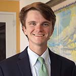 A man with a black suit and green tie stands smiling