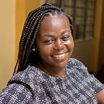 A woman in a gray shirts sits inside while smiling