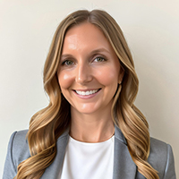 Shea M. Holman Kilian stands wearing a gray blazer and white shirt while smiling