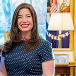 A woman stands in an office and smiles