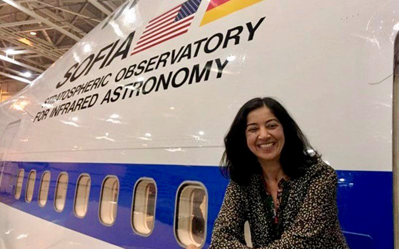 A woman in a black and white top sits in front of a white airborne observatory.
