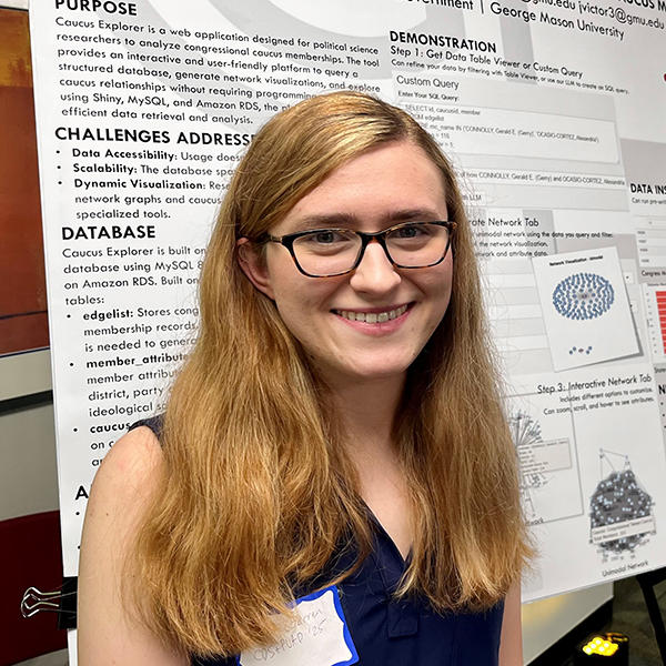A woman with long blonde hair stands and smiles in front of a poster