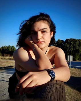 A young woman leaning on a fence gazes at the camera.