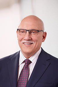 Stu Shea wears a business suit and stands in front of a white background