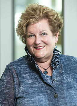 A woman in blue top with a blue necklace.