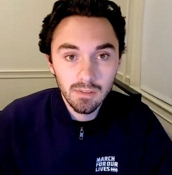 A young man with a short beard in a black shirt looks at the camera.