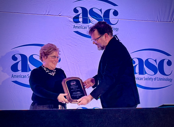 A woman accepts a brown plaque handed to her by a man on a stage.