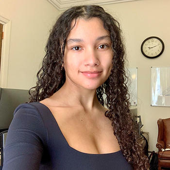 A woman with long curly dark hair in a black top gazes at the camera.