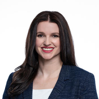 A woman with long hair and wearing a dark jacket smiles at the camera.