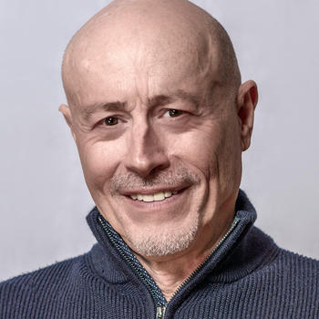 A bald man in a short goatee in a dark zip sweater smiles at the camera.