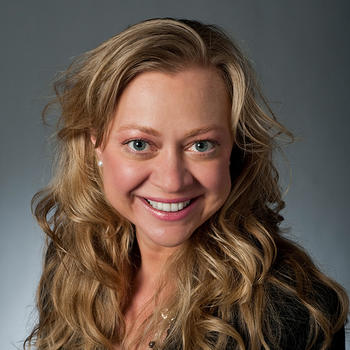 A woman with long blond hair over a dark top smiles at the camera.