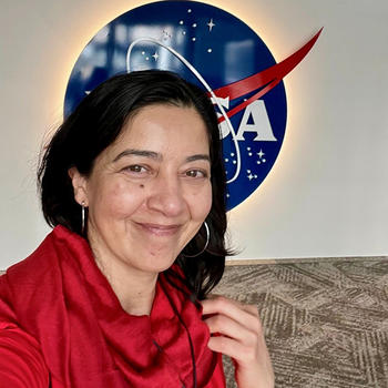 A woman in a red top poses in front of an image of a NASA logo.
